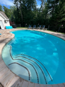 A clean kidney-shaped inground pool with tiled steps and a light blue liner by Christman Pool Service in Portland, ME.