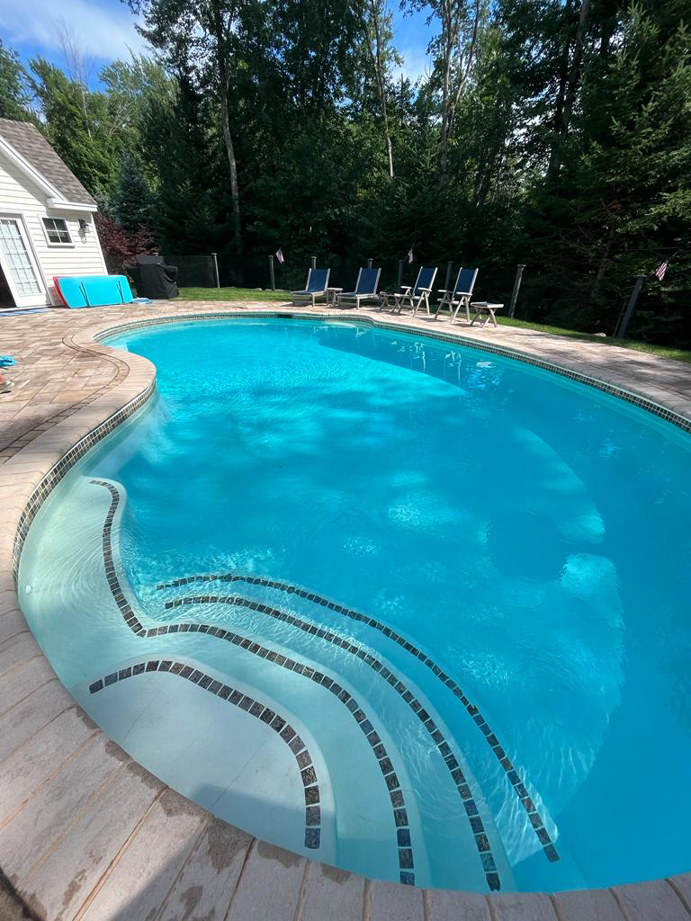A clean kidney-shaped inground pool with tiled steps and a light blue liner by Christman Pool Service in Portland, ME.