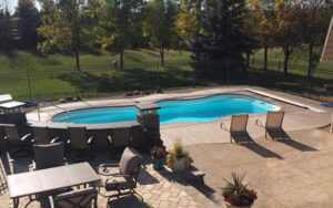 An aerial view of a kidney-shaped swimming pool with surrounding patio furniture and landscaping by Backyard Escapes by Kerner Pools & Spas in Bismarck, ND.