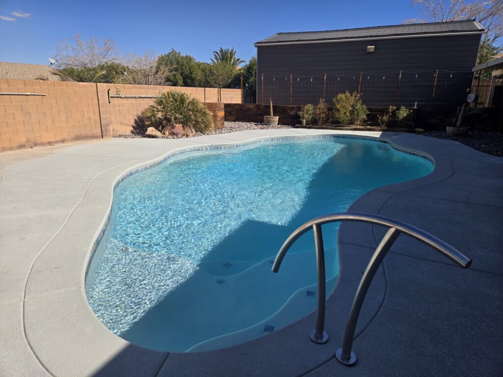 A beautiful kidney-shaped swimming pool with clear blue water and concrete decking by Fix A Pool in Las Vegas, NV