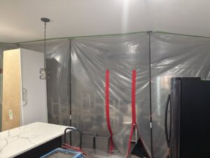 Plastic containment barriers and a dehumidifier set up in a kitchen for water damage restoration by New Method Restoration in Edison, NJ.