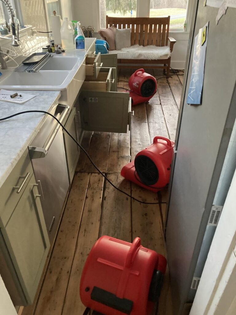 Red drying equipment set up on a wooden floor in a kitchen for water damage drying by CleanBright Surface Restoration in Latham, NY.