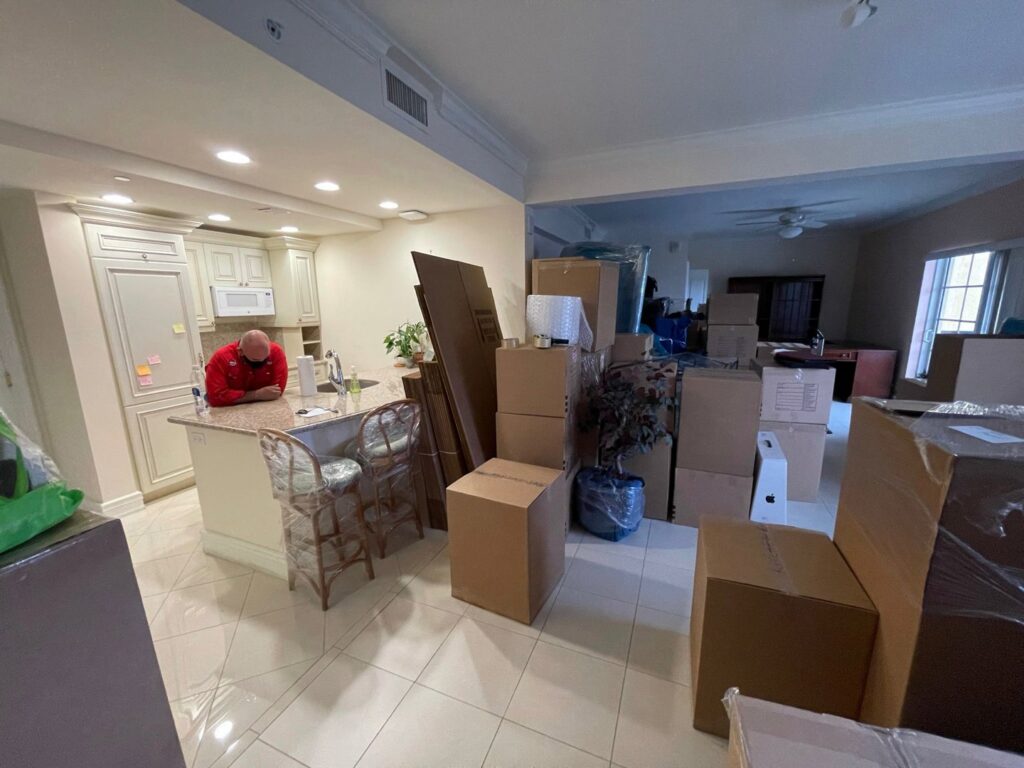 A kitchen and living room area filled with packed moving boxes and wrapped items during a move by Orellana AV Moving in Miami, FL.
