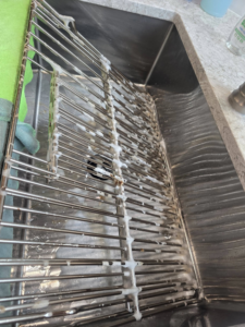 A kitchen sink grate being cleaned with foaming cleanser by Wonderful Laura Cleaning in Aurora, IL.