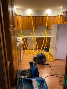 A kitchen undergoing structural drying with yellow tubes inserted into cabinets and floor by Water Damage Pro in Minneapolis, MN