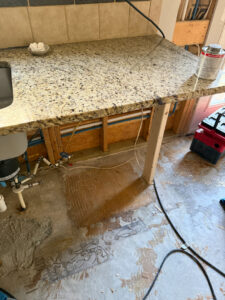 A kitchen with exposed subfloor and pipes undergoing water damage remediation by Triangle Restoration in Raleigh, NC.
