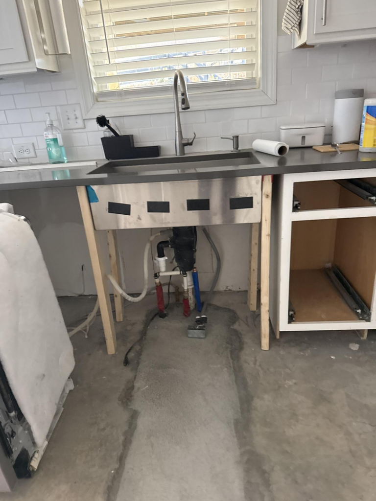 A kitchen undergoing water damage remediation with a temporary sink and exposed wet concrete floor by Triangle Restoration in Raleigh, NC.