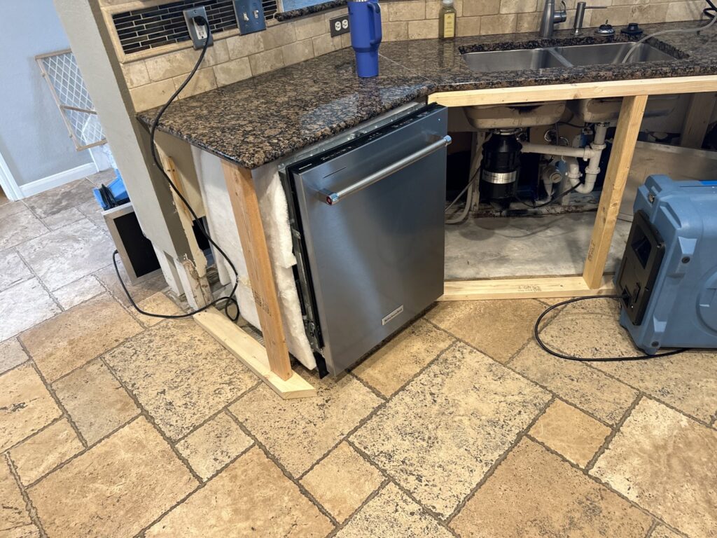 A kitchen area with a dishwasher removed to address a water leak, with a drying fan from Elements of Restoration in Denver, CO.