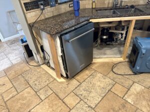 A kitchen area with a dishwasher removed to address a water leak, with a drying fan from Elements of Restoration in Denver, CO.