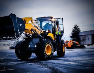 A yellow Komatsu front-end loader with an operator at a commercial snow removal job site for Appleton Snow Removal in Appleton, WI.