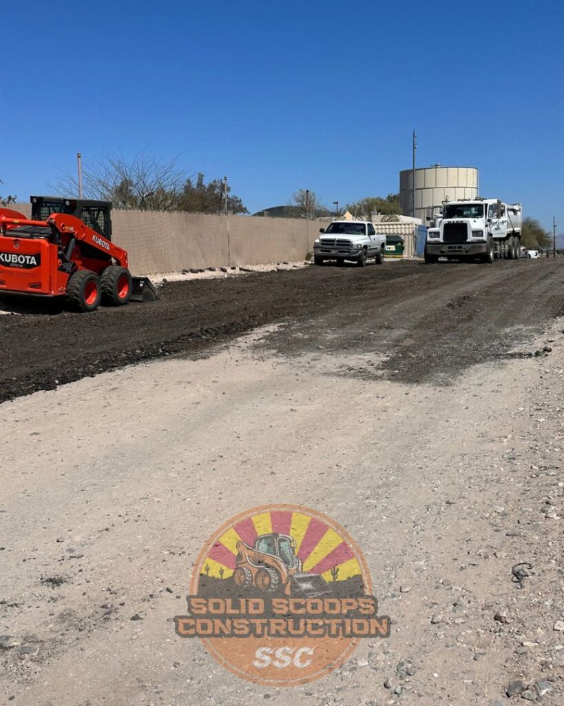 A skid steer performing land clearing and grading on a dirt road for Solid Scoops Construction in Tucson, AZ.