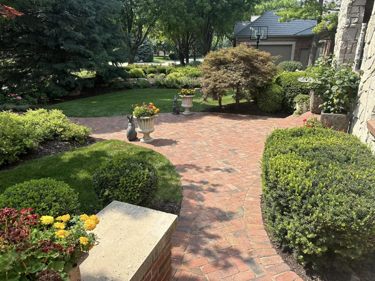 A beautifully landscaped front yard featuring a brick patio, manicured lawn, and healthy shrubs by Mitera Landscaping in Papillion, NE.