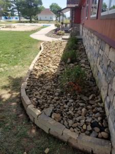 A neatly landscaped rock bed with small plants and a well-maintained lawn by Full Throttle landscapes and lawn care in Port Orchard, WA.