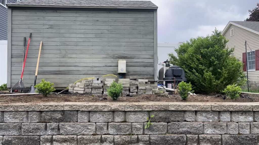 Landscaping tools next to a prepared garden bed with new plants by Steele Lawns in Portland, ME.