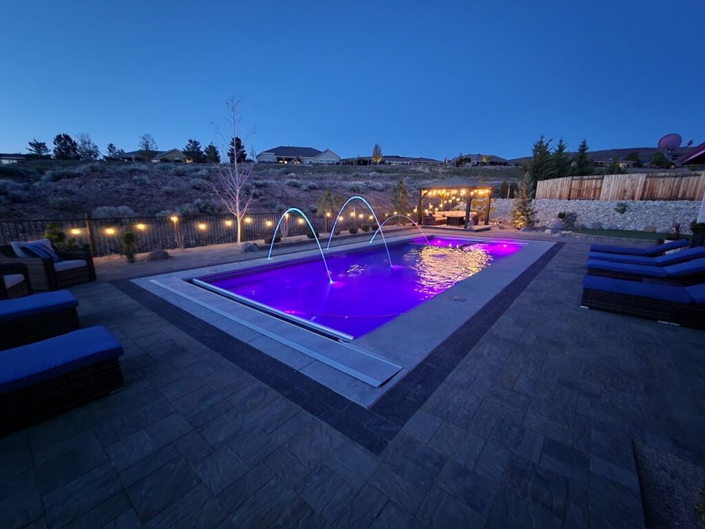 A large backyard pool with vibrant purple lighting and elegant water features, surrounded by patio furniture, by Battle Born Pool & Spa in Sparks, NV.