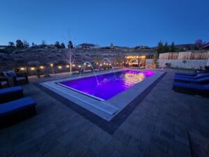 A large backyard pool with vibrant purple lighting and elegant water features, surrounded by patio furniture, by Battle Born Pool & Spa in Sparks, NV.