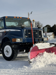A large blue snow plow truck actively pushing and clearing snow from a road for Eric's Winter & Landscape Services in Appleton, WI