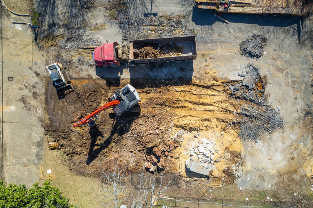 Panoramic view of a large commercial building undergoing demolition with an excavator on site by Nuckles Services in Birmingham, AL