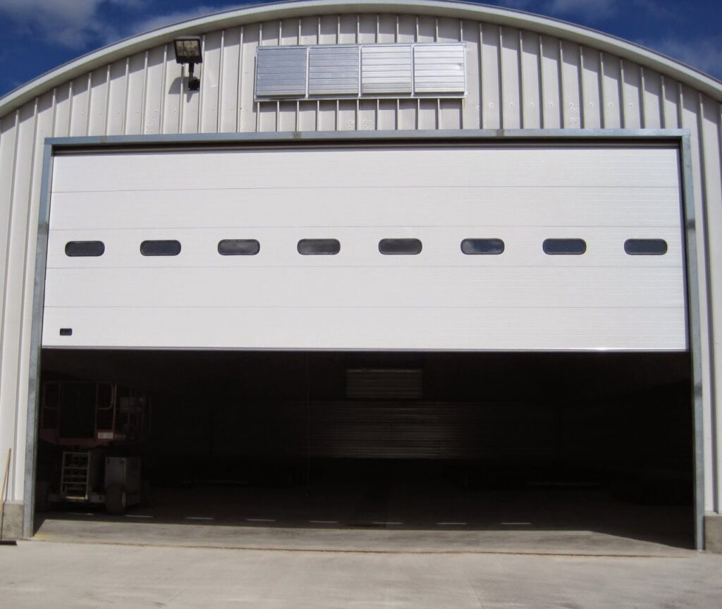 A large white commercial garage door, partially open, installed in a metal building by PS GARAGE DOORS in Grand Forks, ND