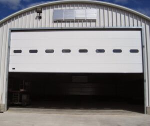 A large white commercial garage door, partially open, installed in a metal building by PS GARAGE DOORS in Grand Forks, ND