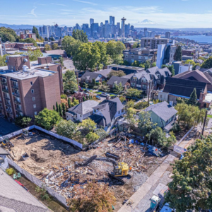 A large demolition site with an excavator and debris, with the Seattle skyline in the background, by Rainstate Earthworks in Auburn, WA.