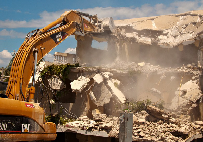 A large excavator demolishing a multi-story concrete building, demonstrating Torrado Demolition's capabilities in Houston, TX.