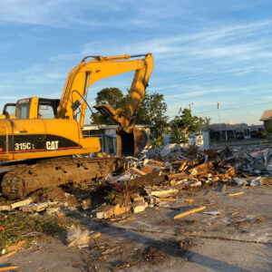 A large excavator working on a pile of demolition debris for New Wave Concepts, a demolition contractor in Cape Coral, FL.