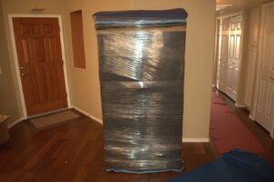 A large piece of furniture wrapped in protective blankets and plastic in a hallway by Moving Pros LLC in Surprise, AZ.