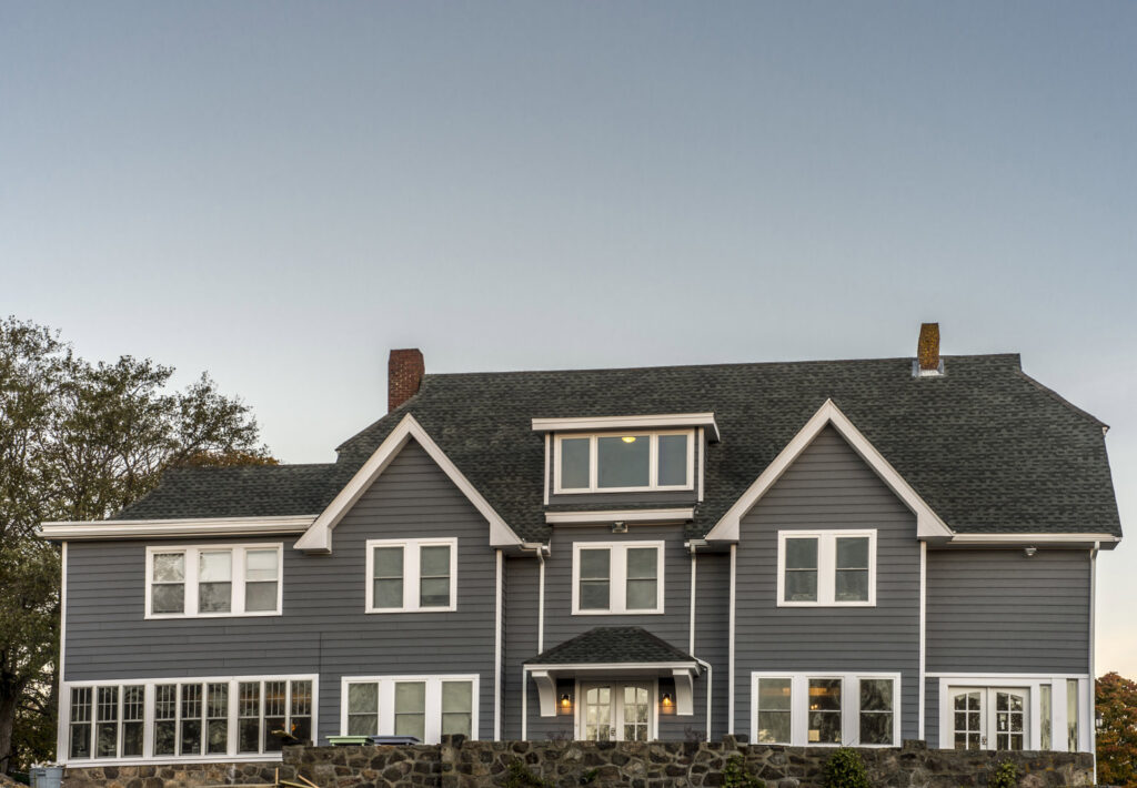 A large, modern grey house featuring newly installed siding and white trim by United Home Experts in Ashland, MA