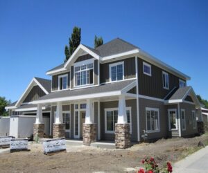 A large, beautiful house with dark green horizontal siding and sturdy stone pillars, a project by New Look Siding in Midvale, UT.