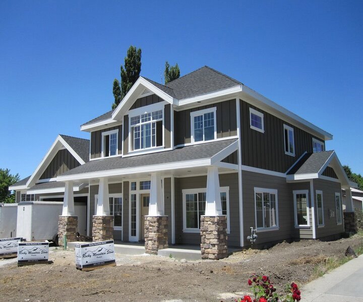 A large, beautiful house with dark green horizontal siding and sturdy stone pillars, a project by New Look Siding in Midvale, UT.