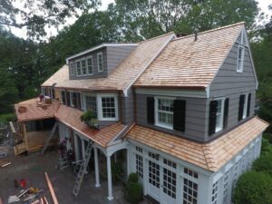 A large house undergoing renovation, featuring gray shingle siding and new cedar shake roofing by JM Roofing & Siding in Rogers, AR.