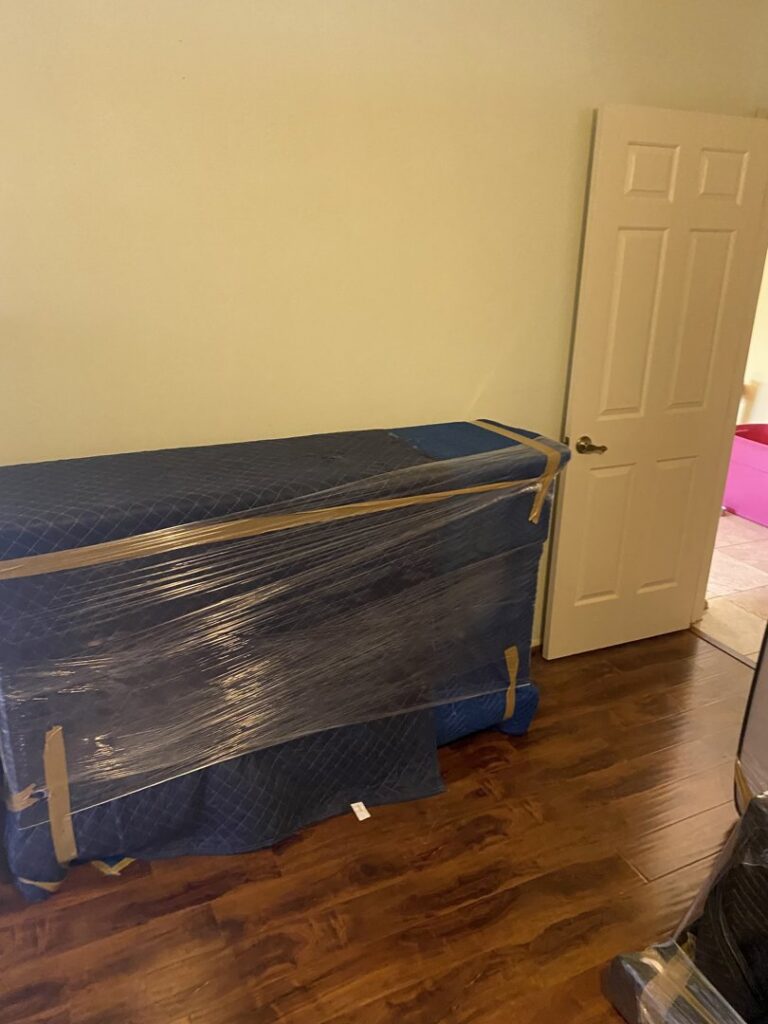 A large piece of furniture wrapped in blue moving blankets and plastic, ready for transport by Moving Marvels in Tucson, AZ.