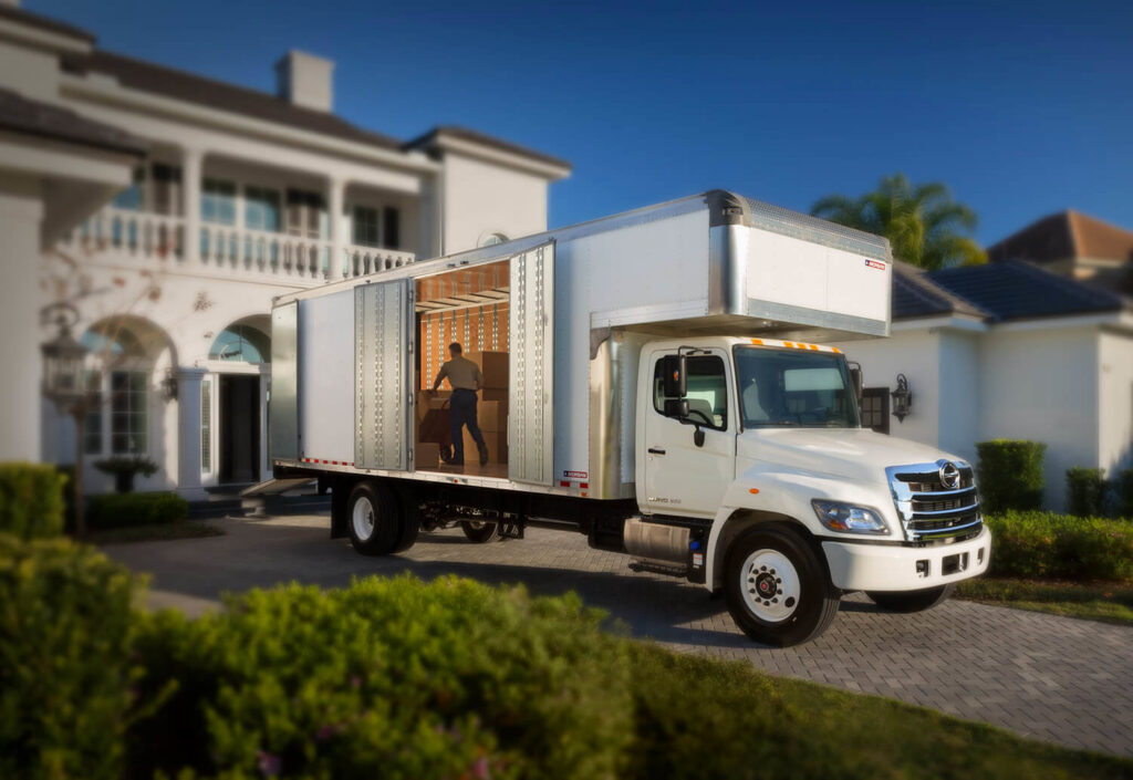 A large white moving truck parked in front of a residential house with a person loading items, provided by Las Vegas Moving Pros LLC in Las Vegas, NV.