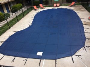 A large, irregularly shaped swimming pool covered with a blue safety cover, demonstrating pool care by Battle Born Pool & Spa in Sparks, NV.