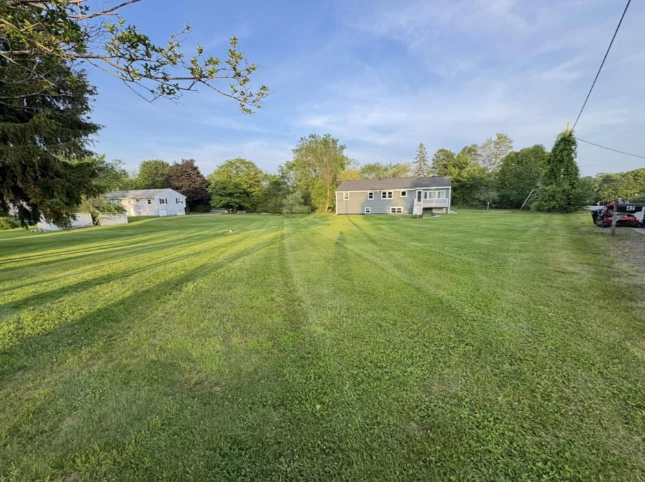 A large, well-maintained residential lawn with fresh mow stripes by Merrily Landscaping LLC in Derry, NH.