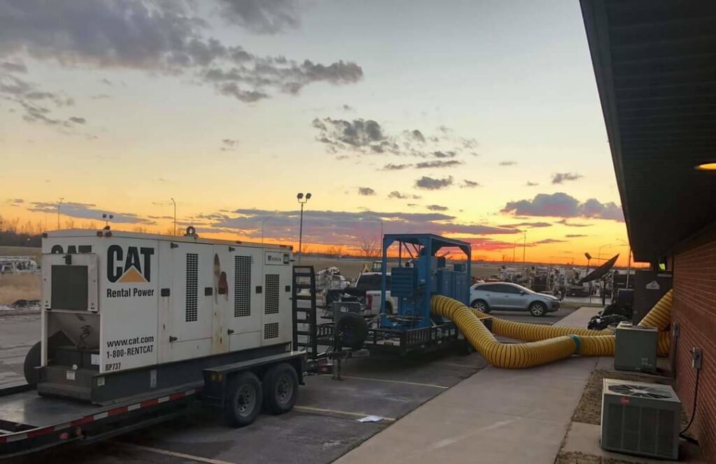 Large-scale water damage drying operation with a generator and yellow ducts leading into a building by Express Restoration in Edmond, OK.