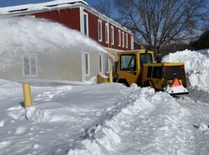 A large yellow snow blower machine actively clearing deep snow away from a building by Alex's lawn care in Rochester, MN.
