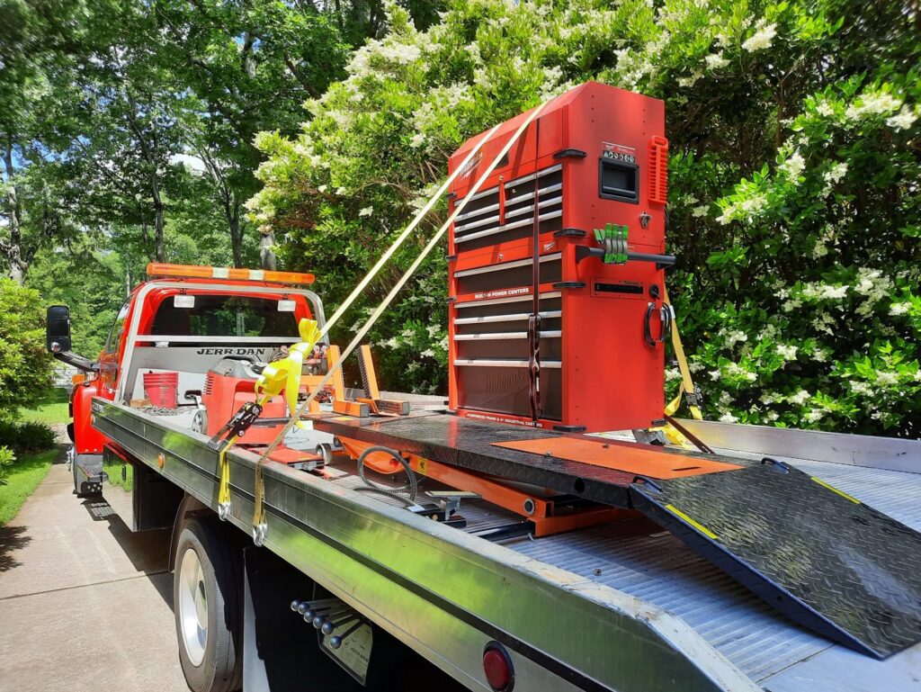A large red toolbox securely transported on a flatbed tow truck by Acme Towing Services in Greenville, SC.