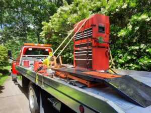 A large red toolbox securely transported on a flatbed tow truck by Acme Towing Services in Greenville, SC.