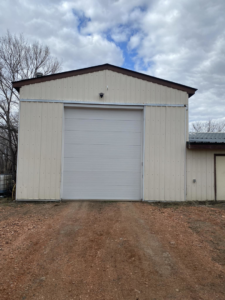 A large white garage door on a beige metal building, installed by PS Garage Doors of Williston, ND.