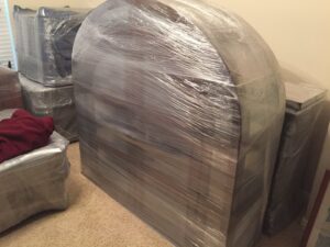 A large piece of furniture, professionally wrapped in plastic by Kingdom Men Movers in Houston, TX, ready for transport.