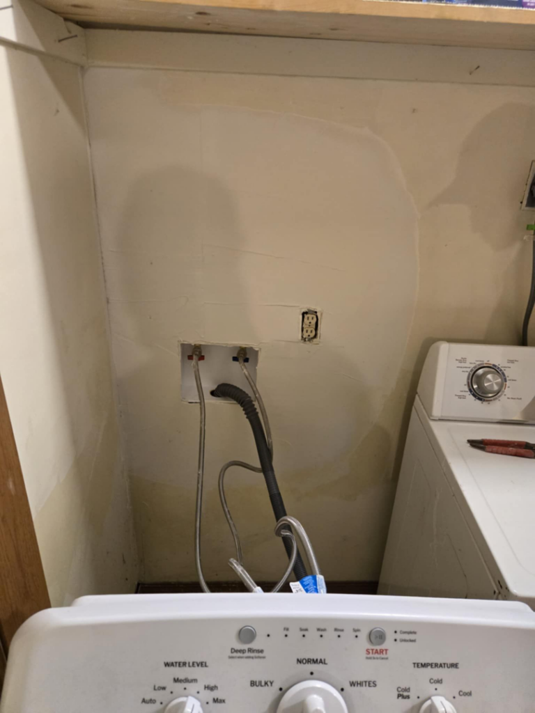 Water stains on a laundry room wall behind a washing machine, showing water damage addressed by Exterior Repair Medics in Manhattan, KS.