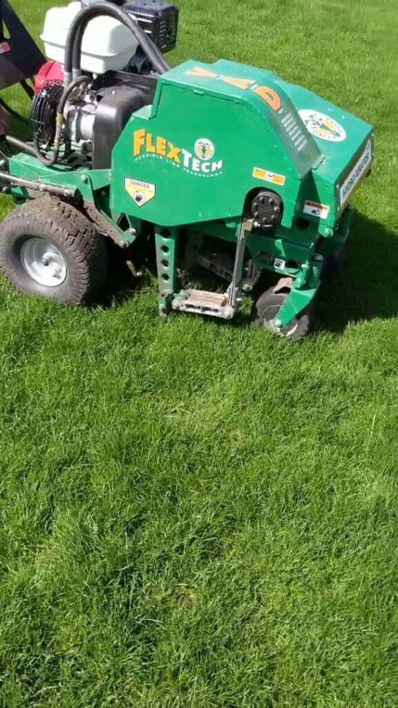 A green FlexTech lawn aeration machine actively working on a healthy lawn, provided by Nice & Precise Lawn Care in Ames, IA.