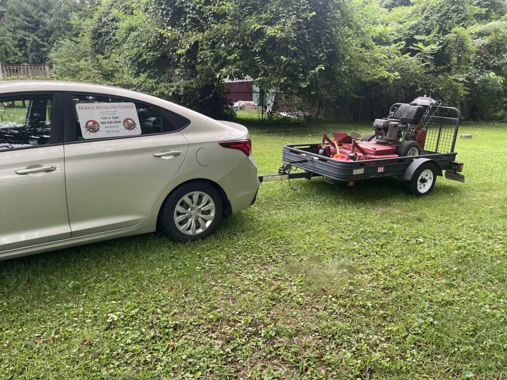 A car towing a trailer with a commercial lawn mower, ready for service by Mike's Lawn Care Service in Dover, DE.