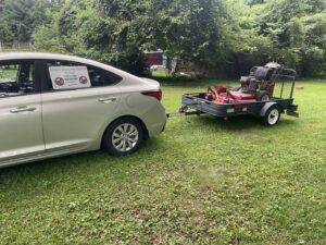 A car towing a trailer with a commercial lawn mower, ready for service by Mike's Lawn Care Service in Dover, DE.