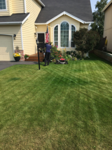 A Leader Lawns professional expertly mowing a residential yard with a push mower in Anchorage, AK.