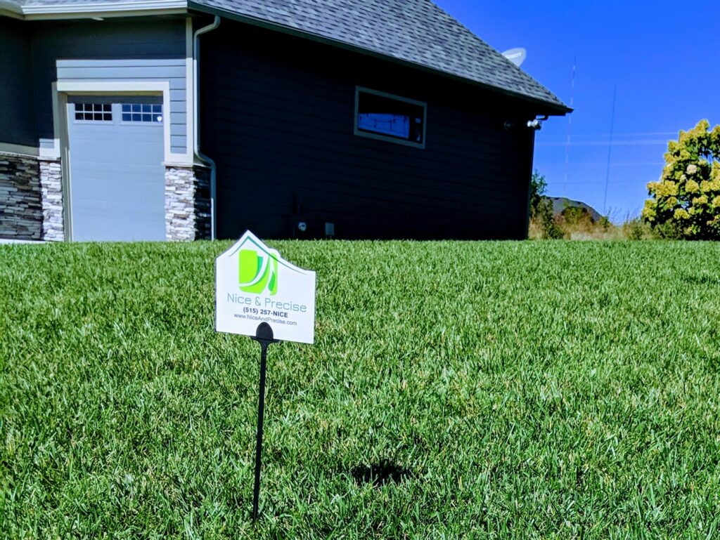 A Nice & Precise Lawn Care sign proudly displayed on a lush, green residential lawn in Ames, IA, indicating professional service.