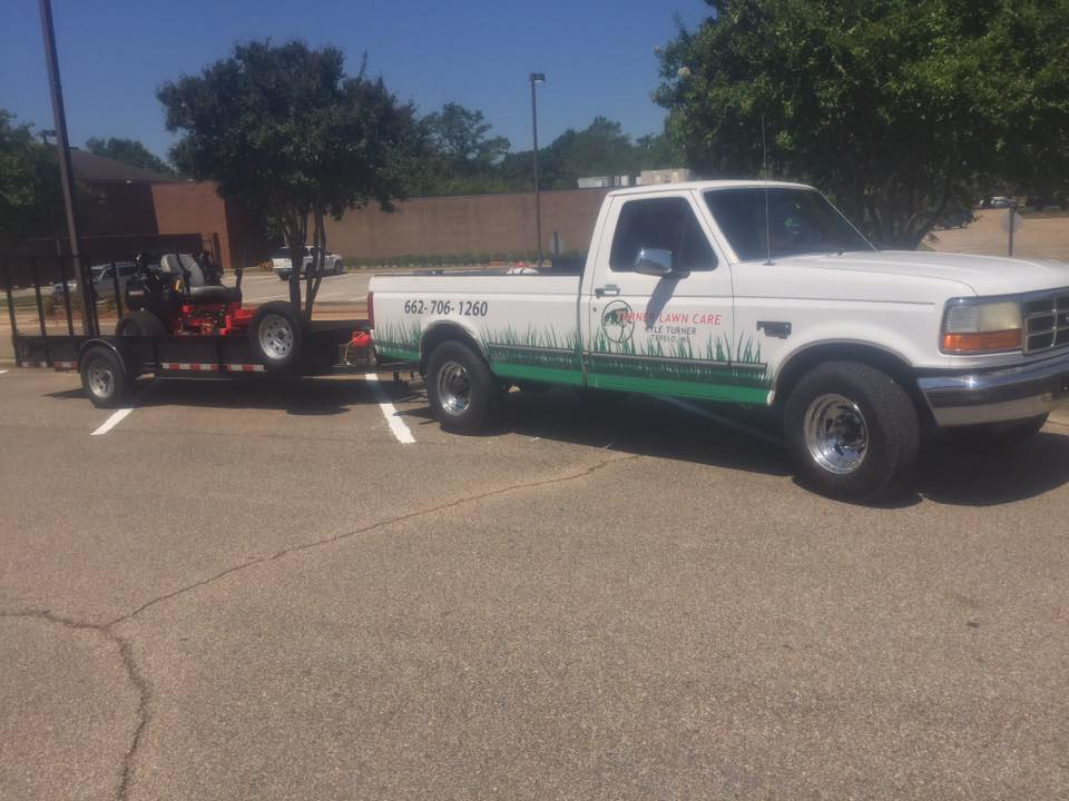 A white pickup truck with Turner Lawn Care branding towing a zero-turn mower in Tupelo, MS.