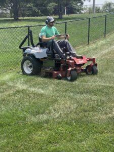 A lawn care worker mowing a sloped residential yard with a riding mower for Heath's Lawn Care in Omaha, NE.